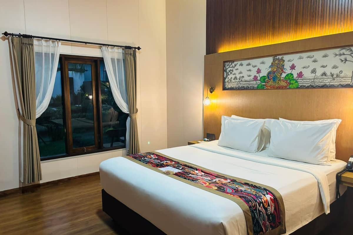 Une chambre d’hôtel avec un grand lit, une fenêtre avec des rideaux, une œuvre d’art accrochée au mur et une table de chevet avec une lampe.