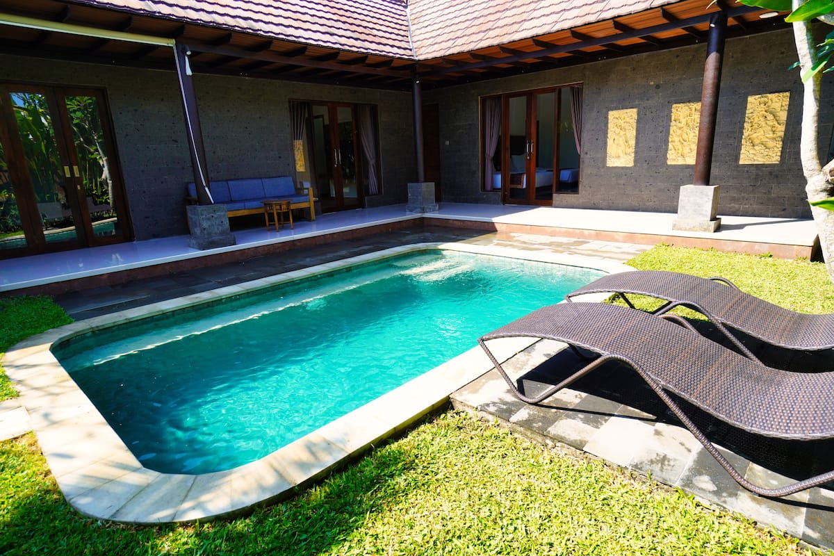 Une piscine avec des chaises longues, un patio couvert et un mur en pierre.