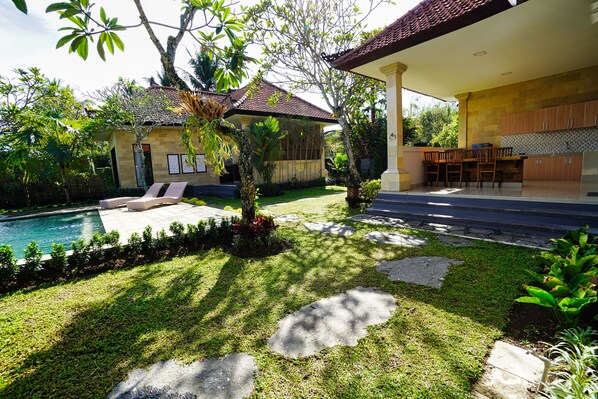 A poolside area with a lounge chair, a small garden with a tree, and a patio with a table and chairs.