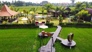 A lush green rice field with a wooden deck, outdoor seating, and a gazebo. - Adil Villa and Resort (Ubud)