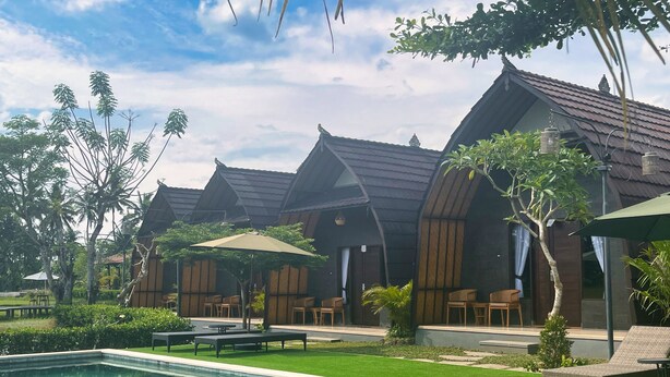 A poolside area with a swimming pool, lounge chairs, and wooden cabanas with thatched roofs. - Adil Villa and Resort (Ubud)