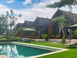 A poolside area with a swimming pool, lounge chairs, and wooden cabanas with thatched roofs.