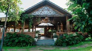 A building with a wooden facade, a covered entrance, and a garden with various plants. - Adil Villa and Resort (Ubud)