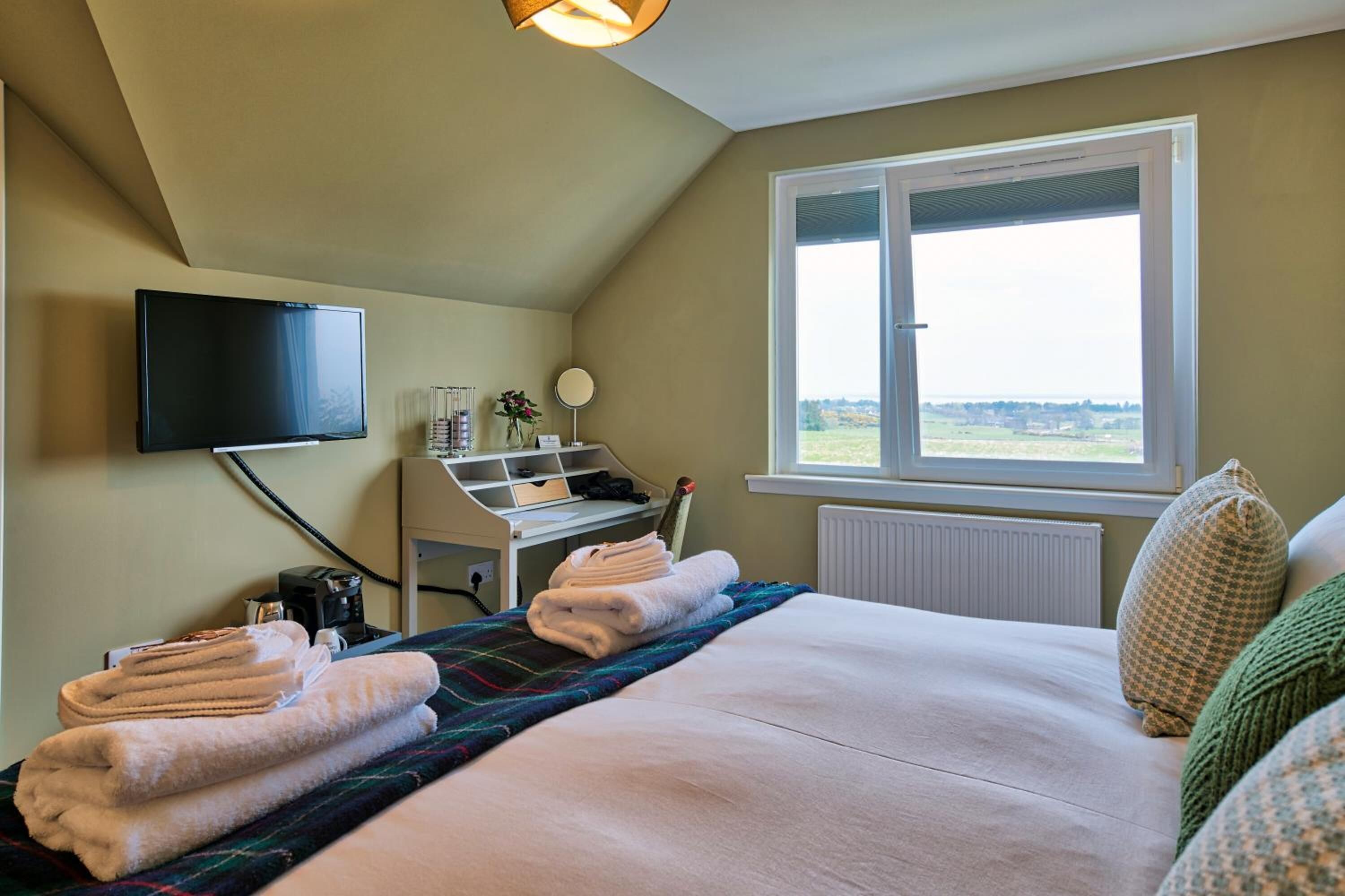 A bedroom with a bed, a desk, a television, and a window with a view.