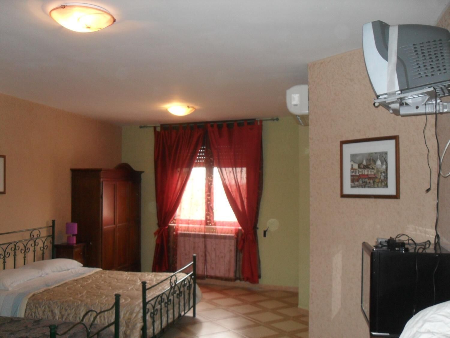 A bedroom with a bed, a wardrobe, a window with red curtains, and a ceiling fan.