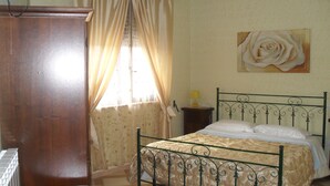 Ein Schlafzimmer mit einem Bett, einem Holzschrank, einem runden Tisch und einem Rosenbild an der Wand.