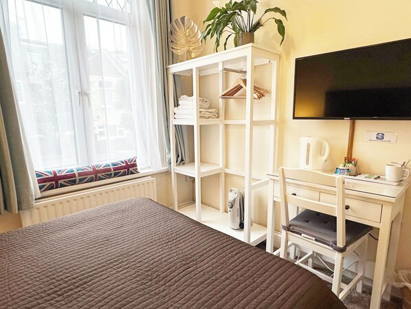 A hotel room with a bed, a desk with a chair, a television, and a radiator.