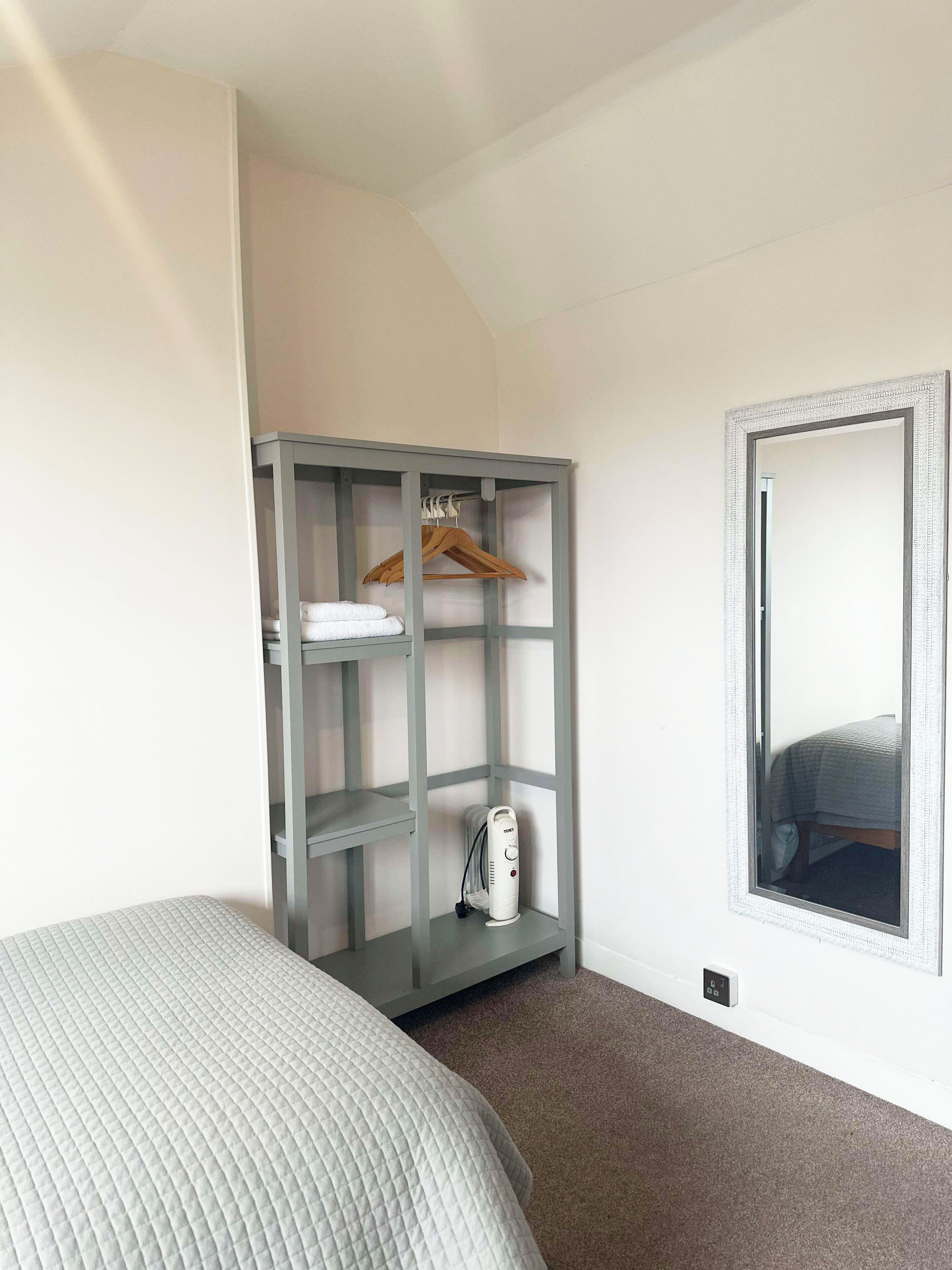 A bedroom with a bed, a grey wardrobe, a heater, and a mirror.