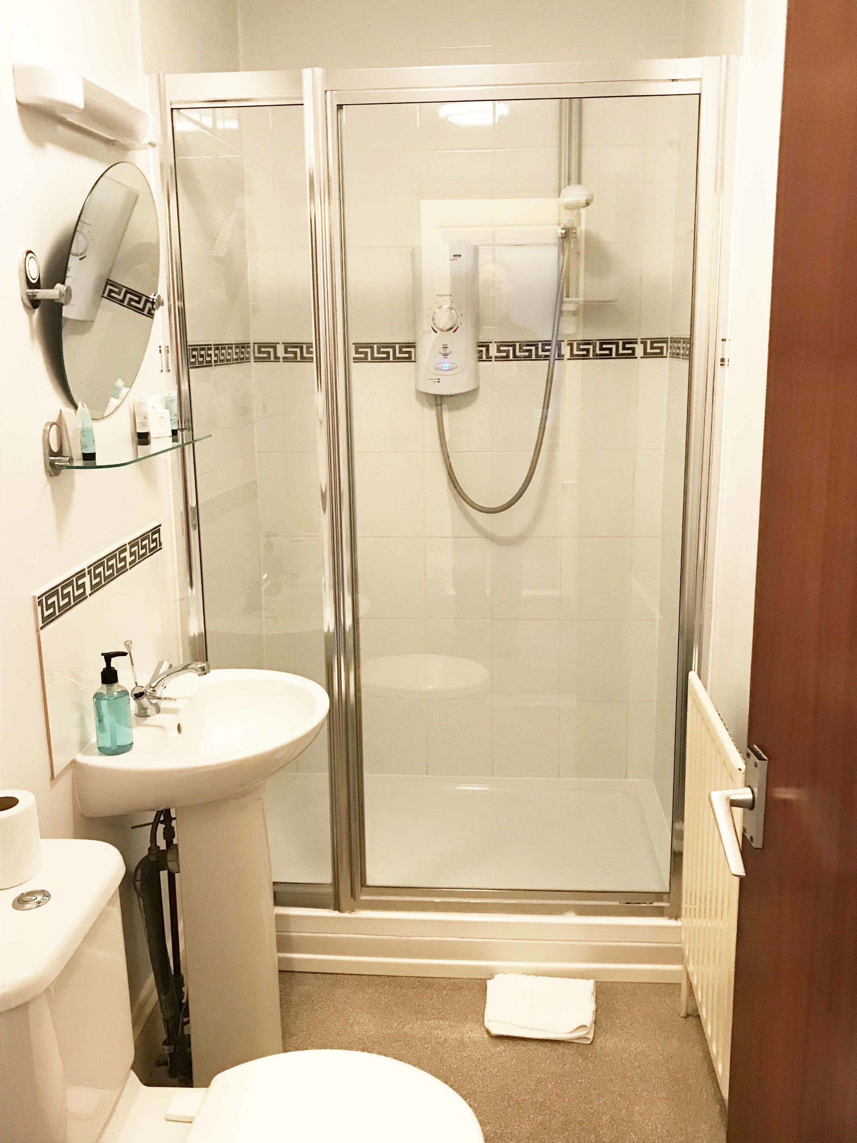Une salle de bain avec une douche à parois de verre, un lavabo blanc, un miroir et des toilettes.