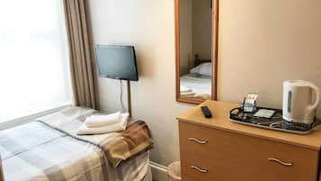 A hotel room with a bed, a bedside table with a remote control, a coffee maker, and a mirror.