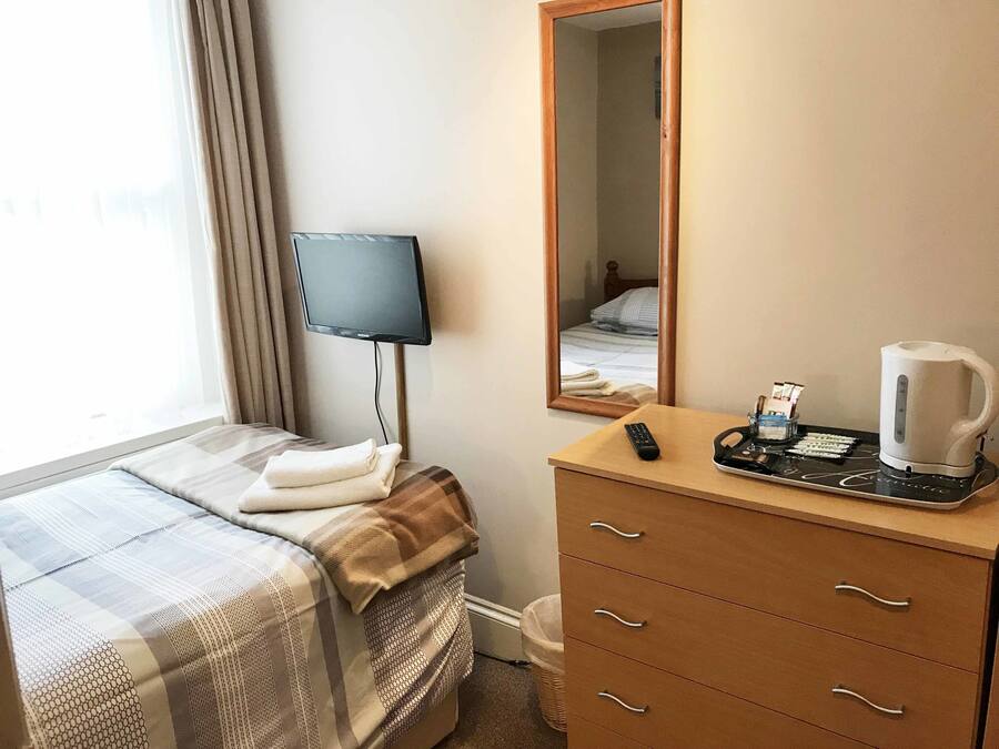 A hotel room with a bed, a bedside table with a remote control, a coffee maker, and a mirror.
