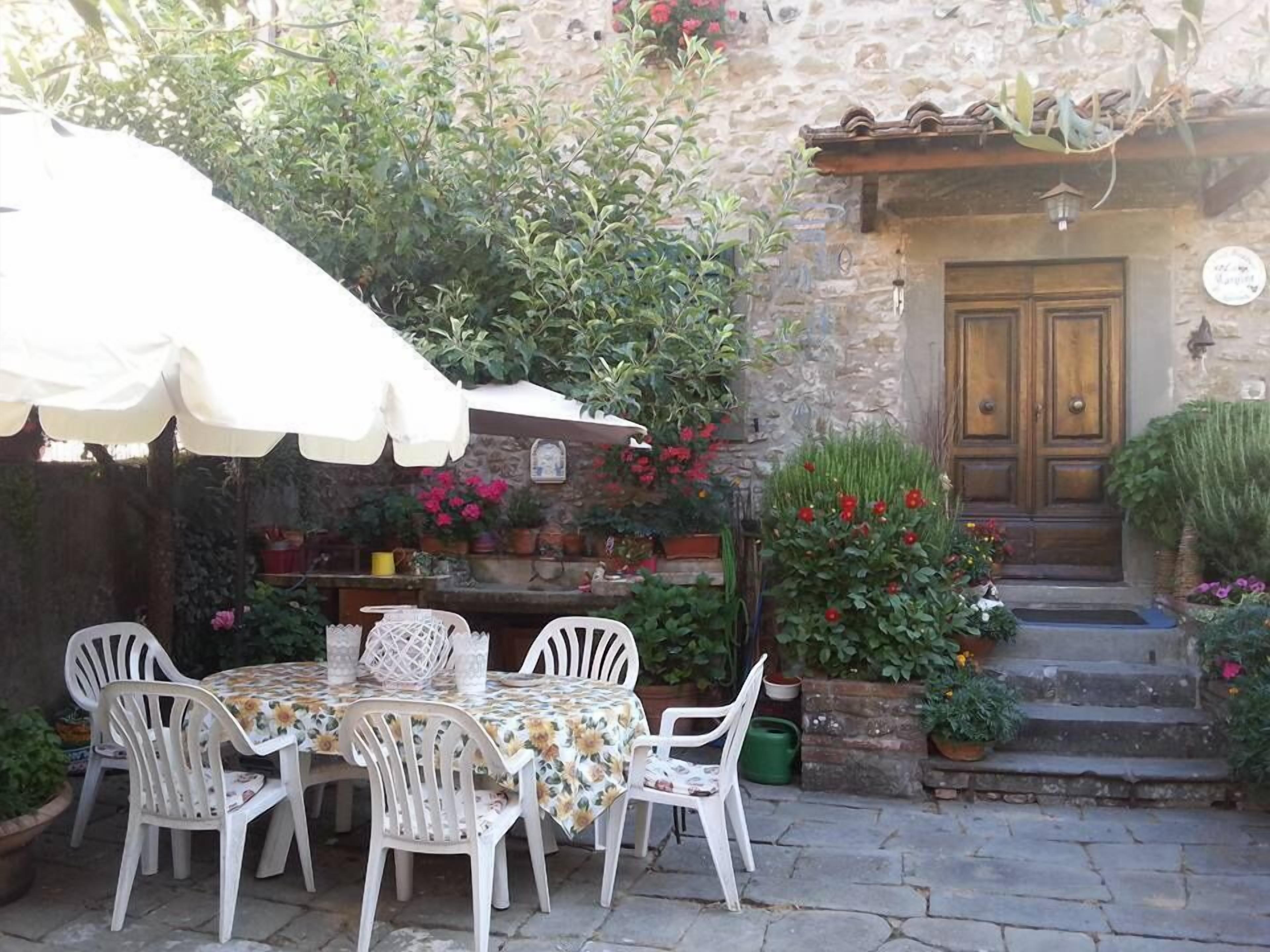 An outdoor patio with a table and chairs, surrounded by potted plants and flowers.