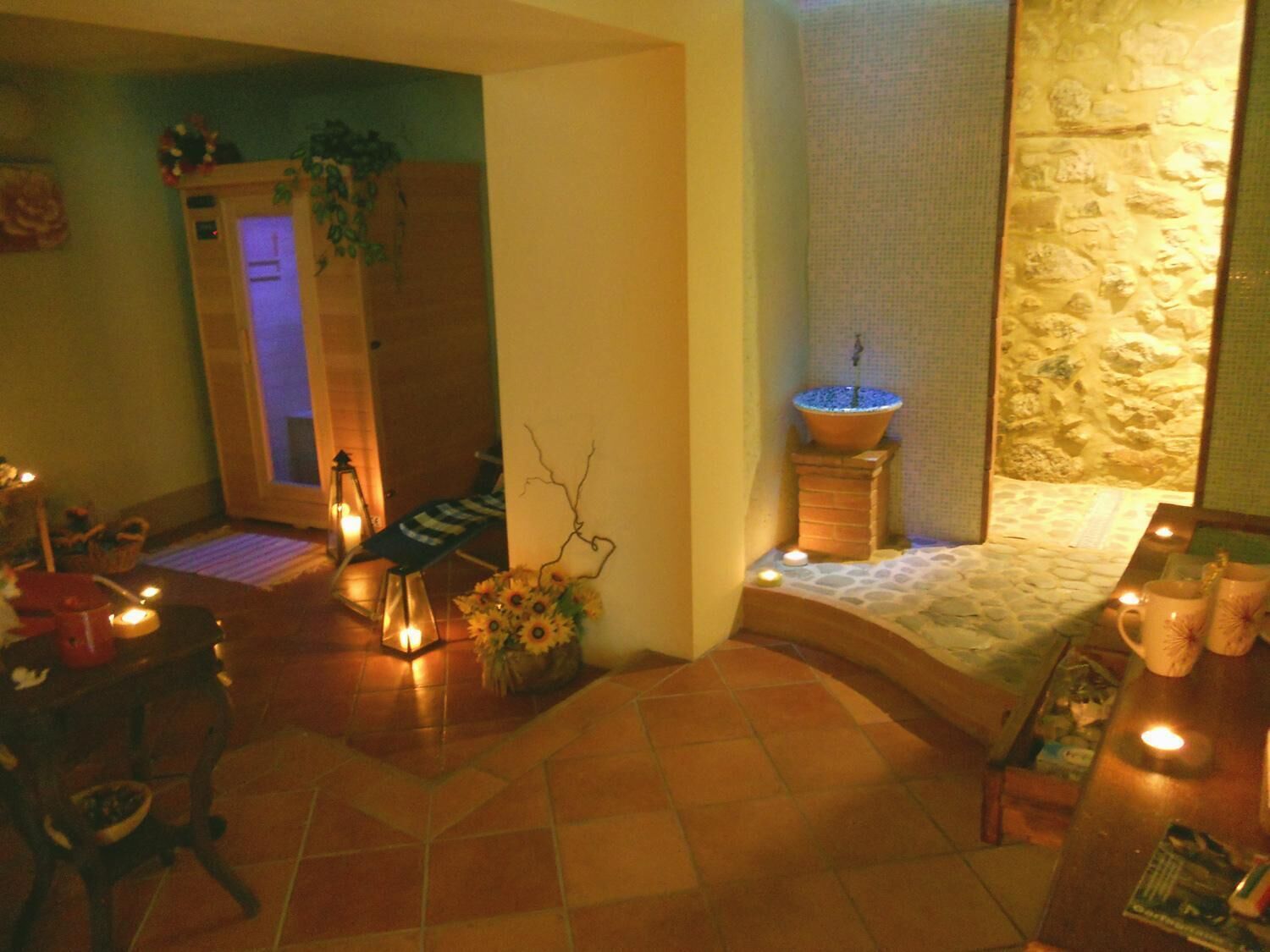 Ein Spa-Raum mit Steinwand, einer Holzbank und einem kleinen Tisch mit Kerzen und Blumen.