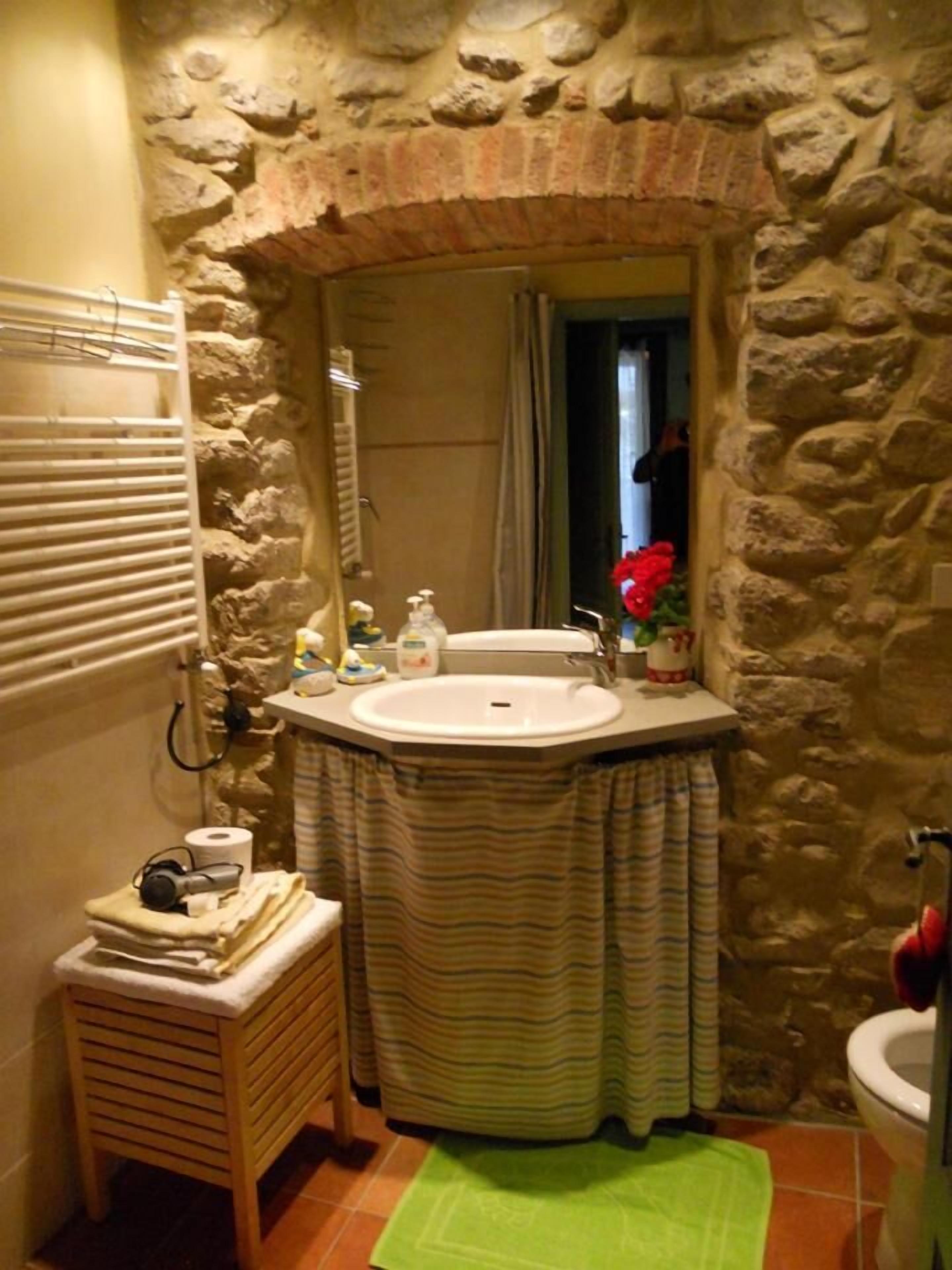 A bathroom with a stone wall, a wooden stool, a green bath mat, and a sink with toiletries.