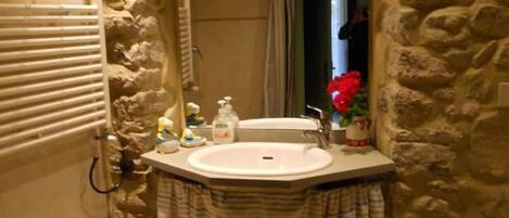 A bathroom with a stone wall, a wooden stool, a green bath mat, and a sink with toiletries.