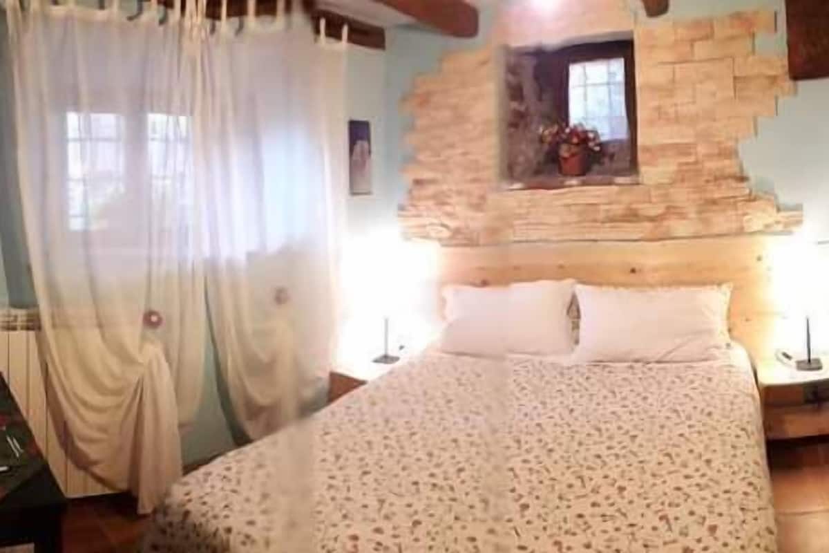Un dormitorio con una cama grande, una mesita de noche, una pequeña mesa y una ventana con vistas.
