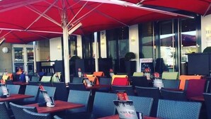An outdoor seating area with red umbrellas, wicker chairs, and tables. - Stadthotel Langenfeld (Langenfeld)