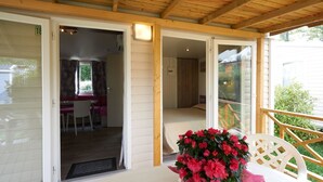 A covered patio area with a table and chairs, a flower arrangement, and a view of the adjacent room with a bed and window. - Camping Baia Verde (Manerba del Garda)