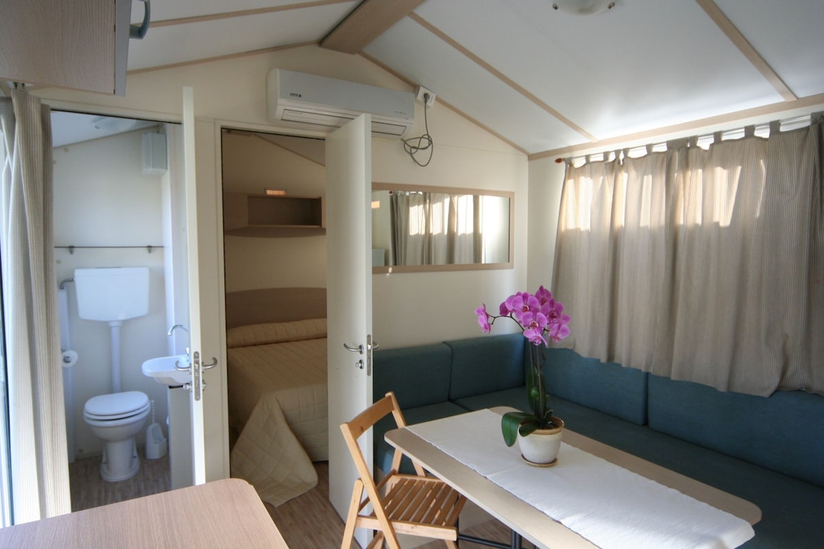 A compact RV interior with a kitchenette, a dining area, and a seating area with a sofa and a table.