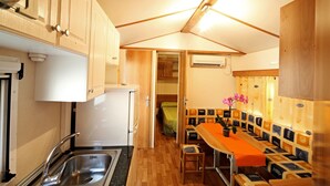 A compact kitchen with a sink, cabinets, and a refrigerator. There is a dining area with a table and benches. - Camping Baia Verde (Manerba del Garda)