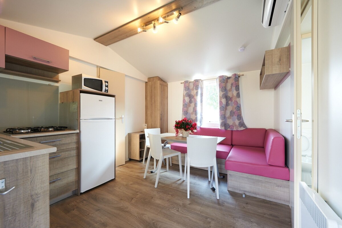A compact kitchen with a refrigerator, microwave, and stove. There is a dining area with a table and chairs, and a pink sofa.