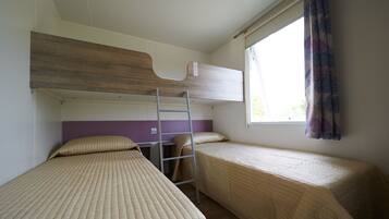 A dormitory room with bunk beds, a ladder, a window with curtains, and a desk with a chair.