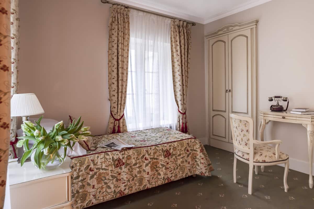 Un dormitorio con cama, escritorio con teléfono, silla, armario y lámpara.