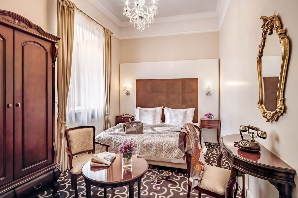 Una habitación de hotel con una cama grande, un armario de madera, una mesa redonda y un teléfono clásico.