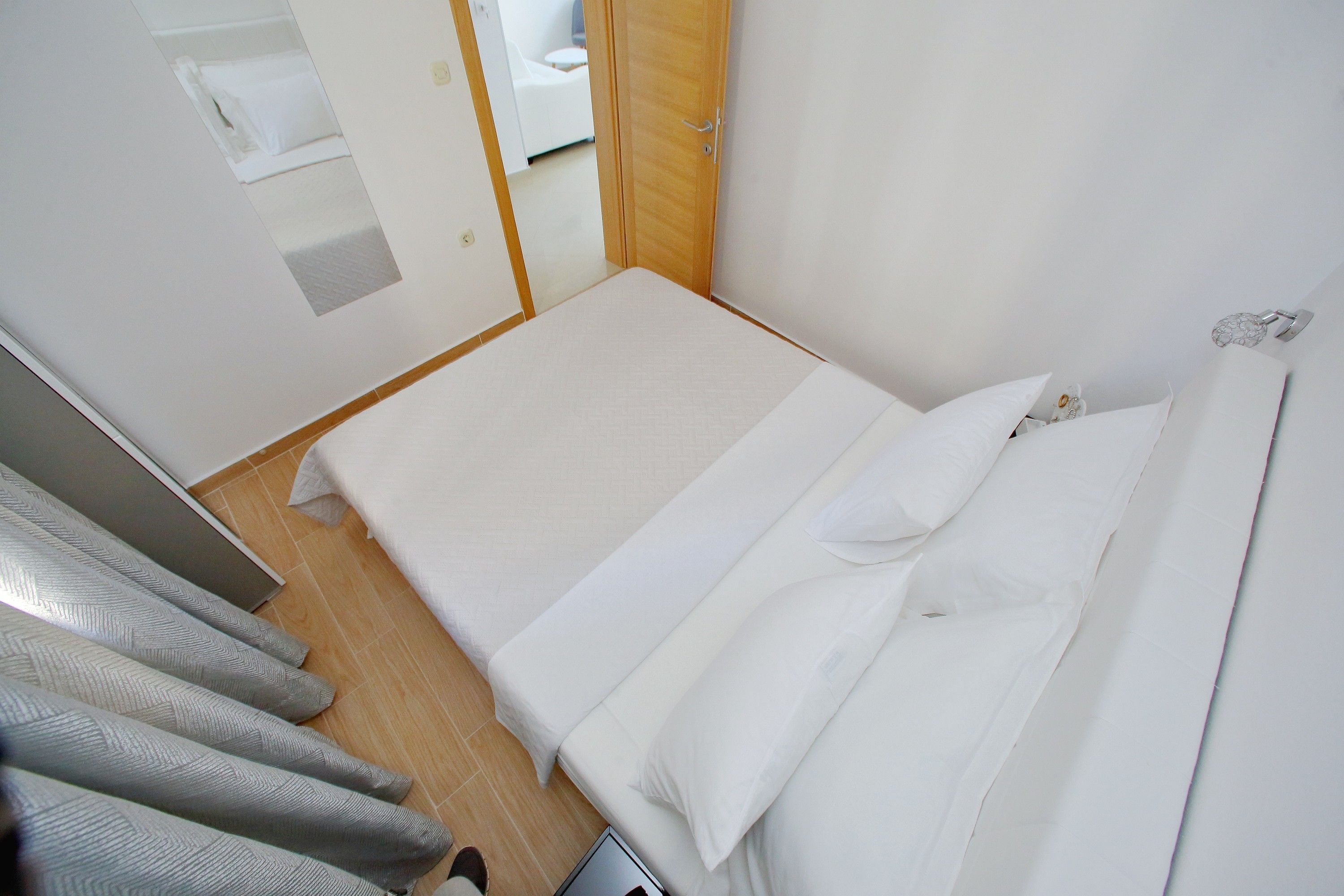 A small, neatly made bed in a room with a wooden floor and white walls.