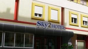 Un hotel chiamato "Sky2 Hotel" con una facciata moderna, ampie finestre e una combinazione di colori rosso e giallo.