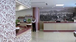 Un'area reception di un hotel dal design moderno, con una parete decorata da un motivo, un'ampia scrivania della reception e un murale raffigurante una vista sulla città sullo sfondo.