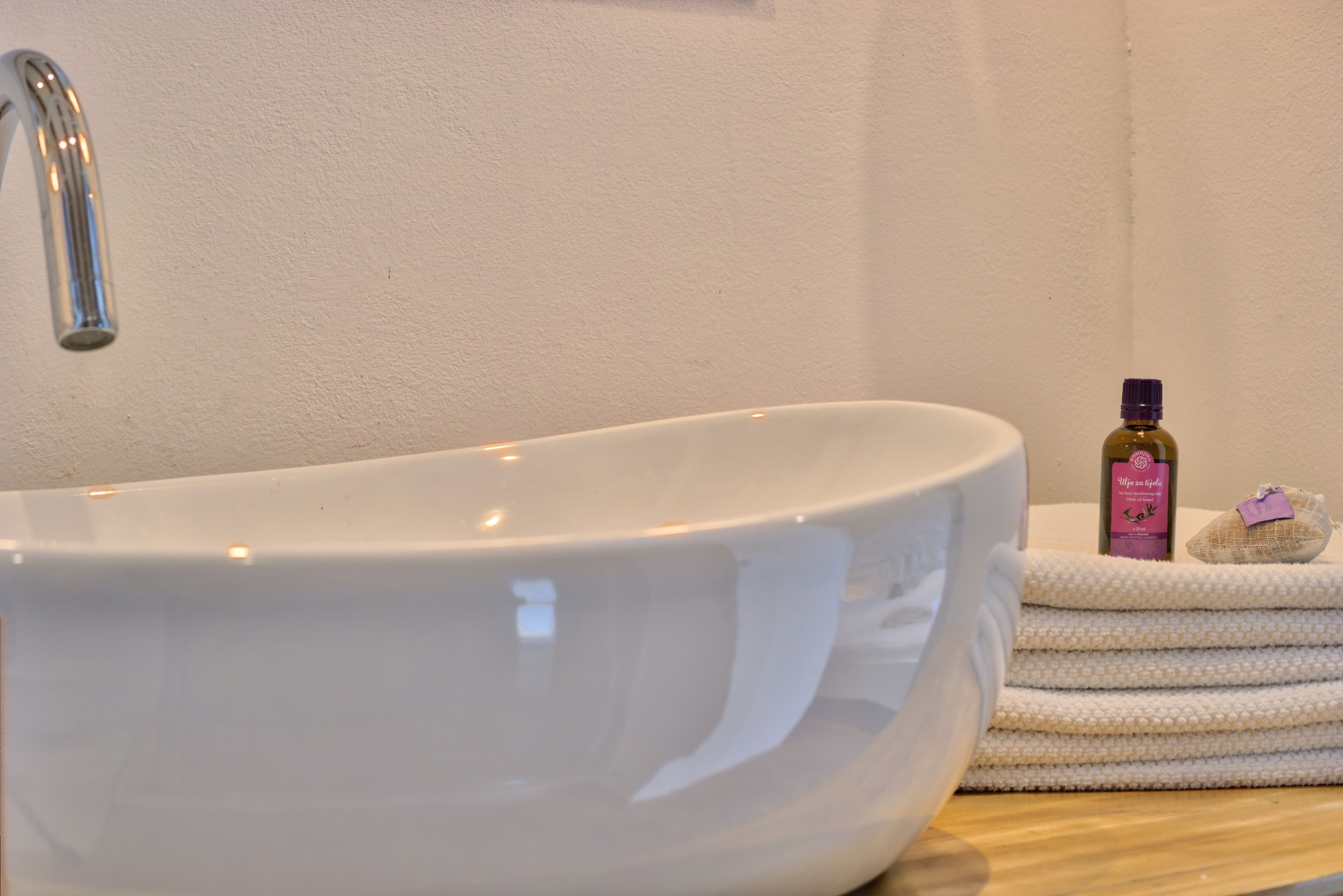 Un lavandino in ceramica bianca con un rubinetto moderno, una bottiglia di sapone profumato alla lavanda e un asciugamano piegato su una superficie in legno.