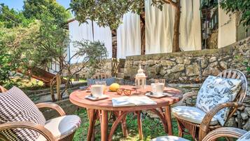 Un espace extérieur aménagé avec des chaises en osier et une table ronde, entouré de verdure et d’un mur en pierre.