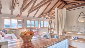 Una cocina moderna con vigas de madera, un ventanal grande y un bol de fruta sobre la encimera.
