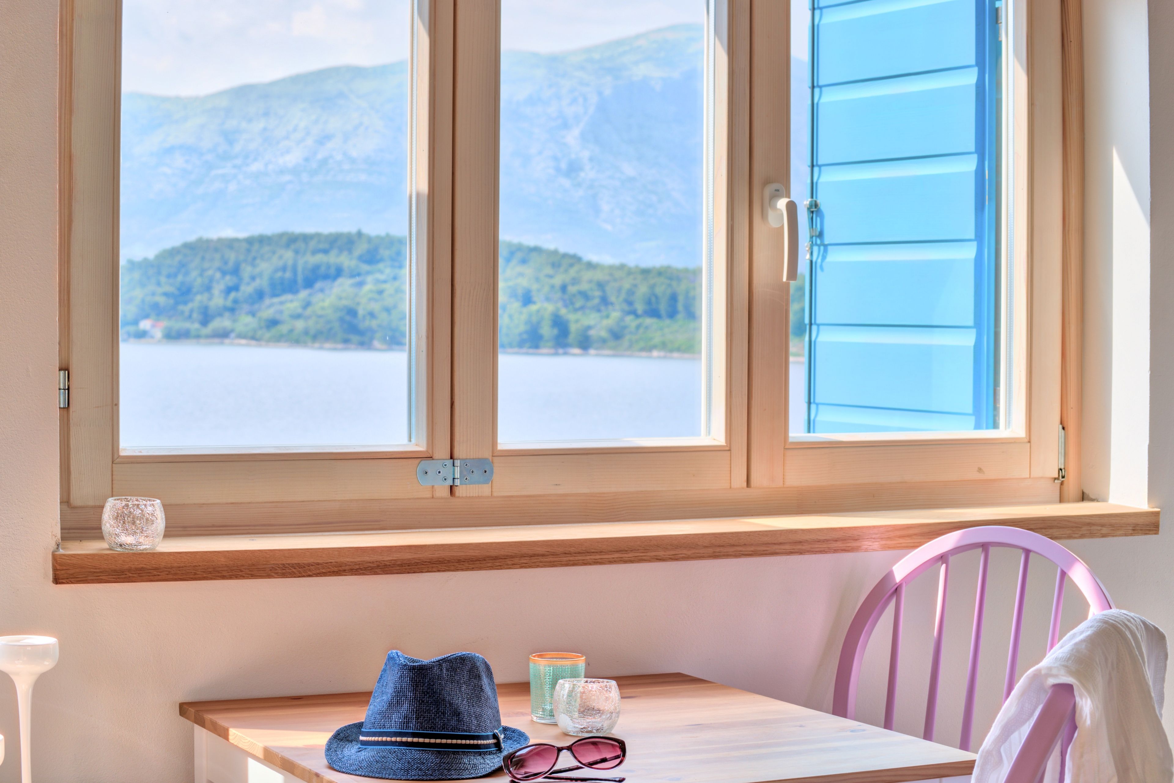 Ein Zimmer mit einem Holztisch, einem Stuhl und einem Fenster mit Blick auf einen See und Berge.