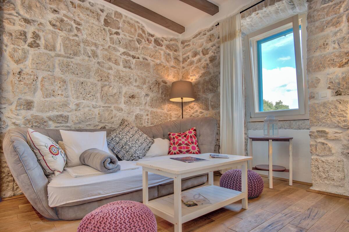 Une pièce chaleureuse avec un mur en pierre, un canapé avec des coussins, une petite table et une fenêtre donnant sur un beau paysage.