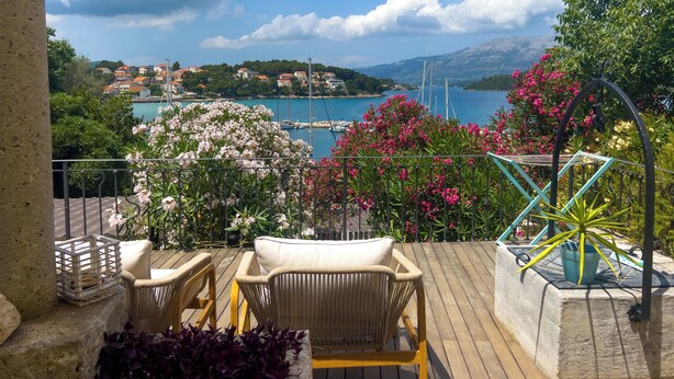 Een balkon met rieten meubilair, uitzicht op een kustplaatsje en een heldere lucht.