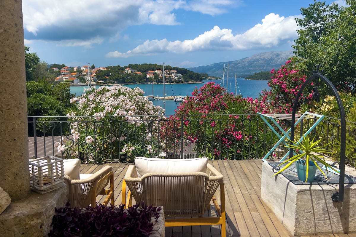 Un balcon agrémenté de meubles en osier, une vue sur une ville côtière et un ciel dégagé.