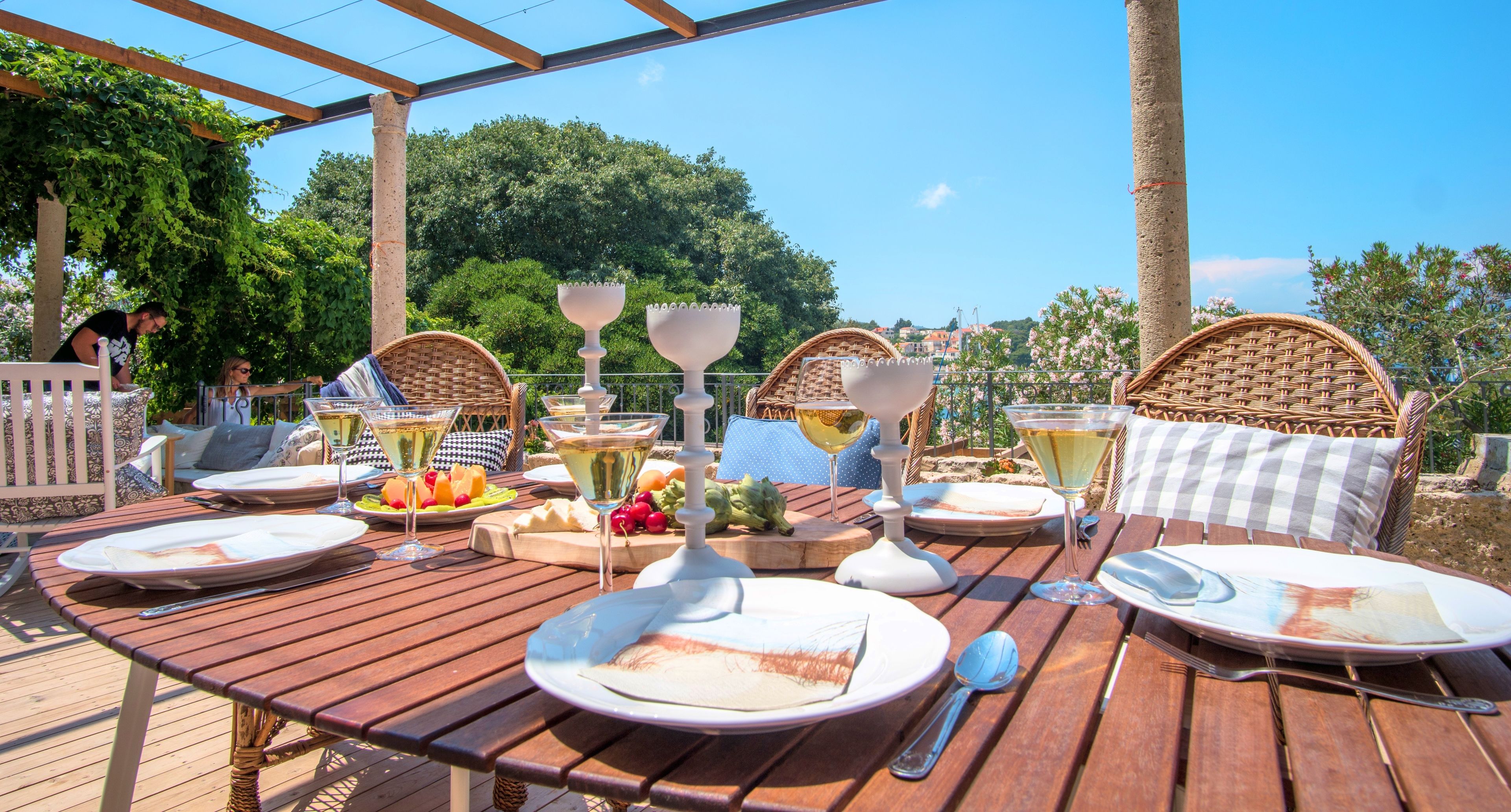 Ein Essbereich im Freien mit Holztischen, Korbstühlen und einer Pergola.