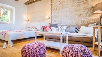 A cozy living room with a stone wall, a white sofa, a brown sofa, and two knitted poufs.