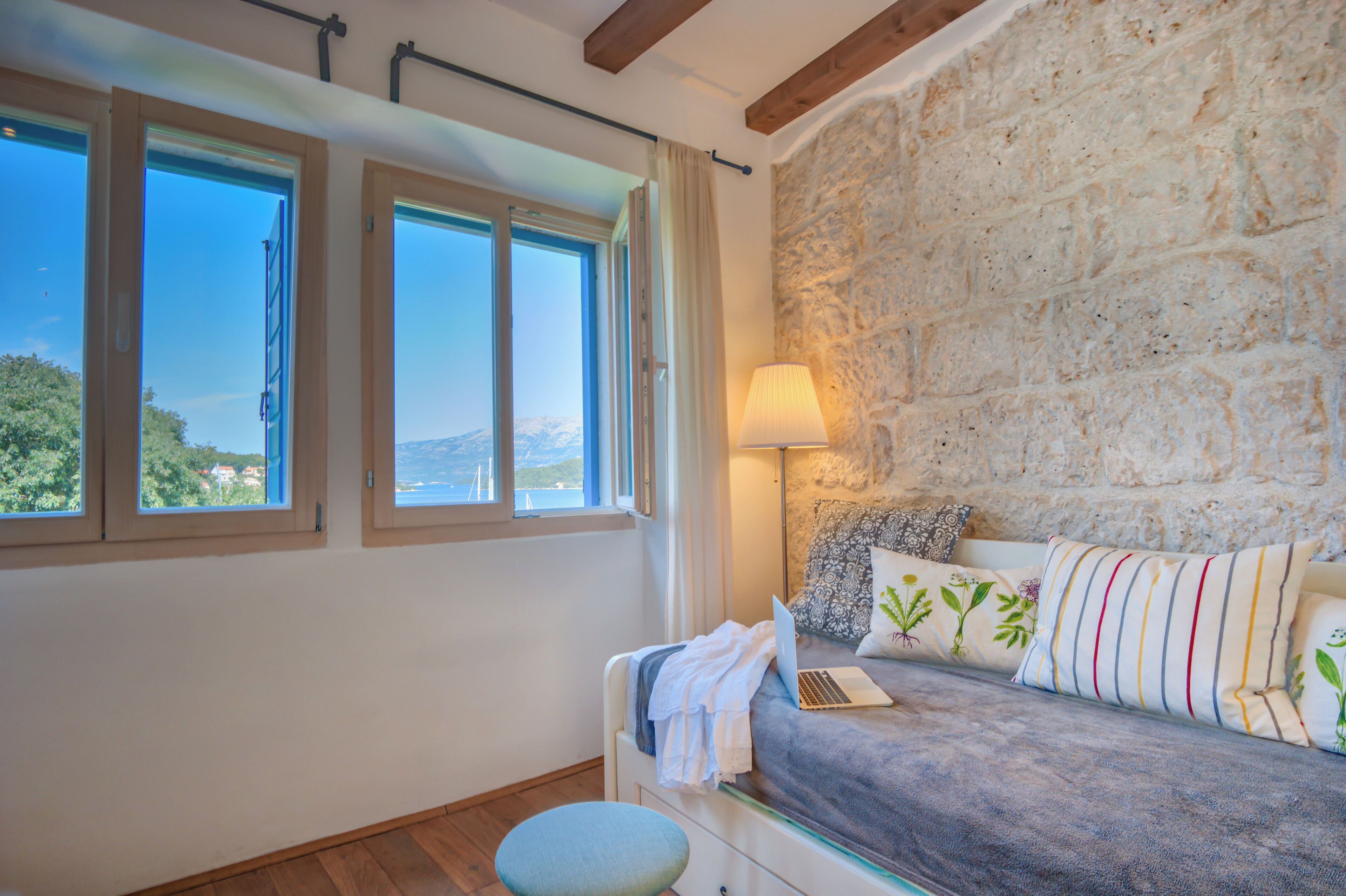 Un dormitorio con pared de piedra, una cama con un ordenador portátil y vista al mar.