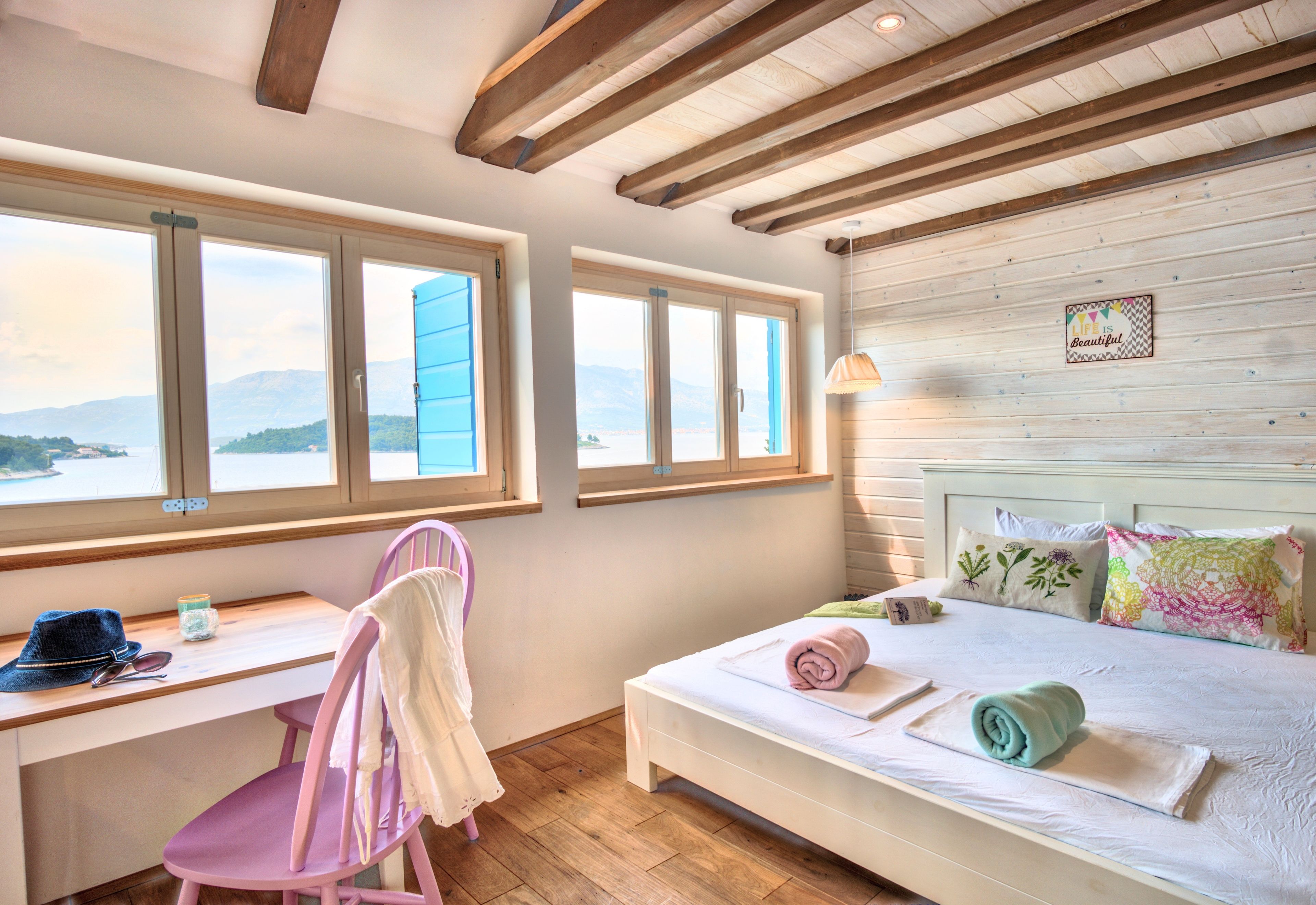 A bedroom with a bed, a desk, and a chair. There are windows with a view of mountains.