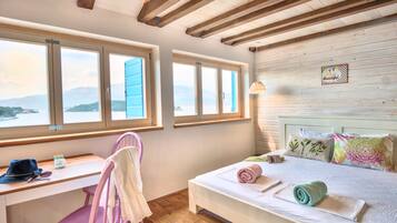 A bedroom with a bed, a desk, and a chair. There are windows with a view of mountains.
