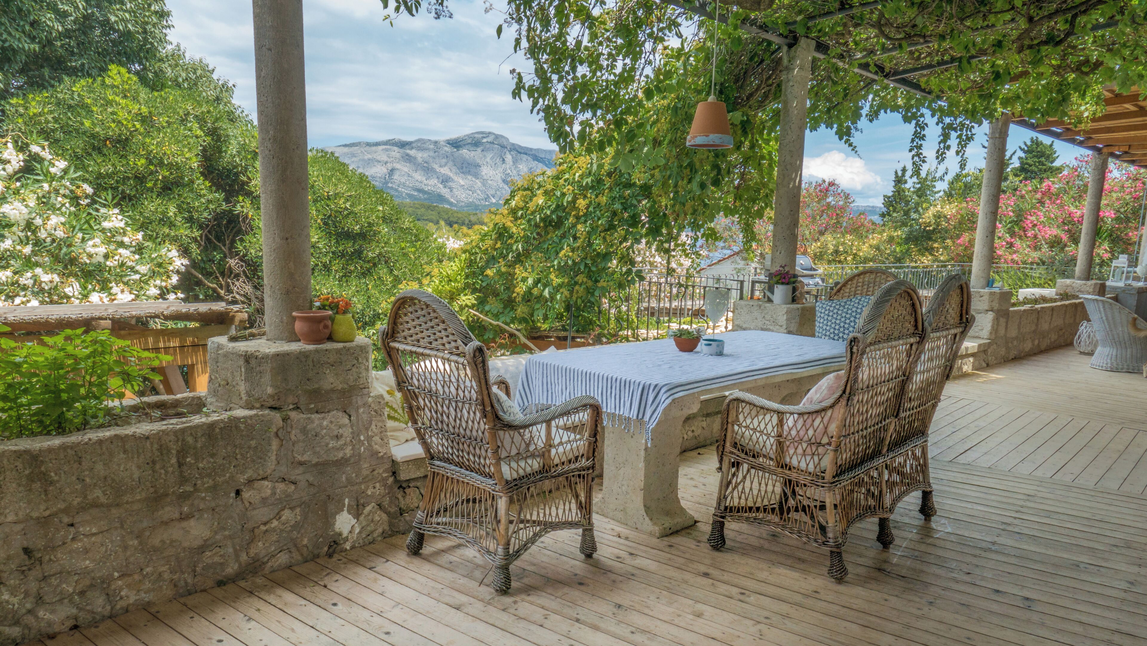 Une terrasse extérieure avec des chaises et une table en osier, entourée de murs en pierre et de plantes en pot, offrant une vue sur un paysage montagneux.