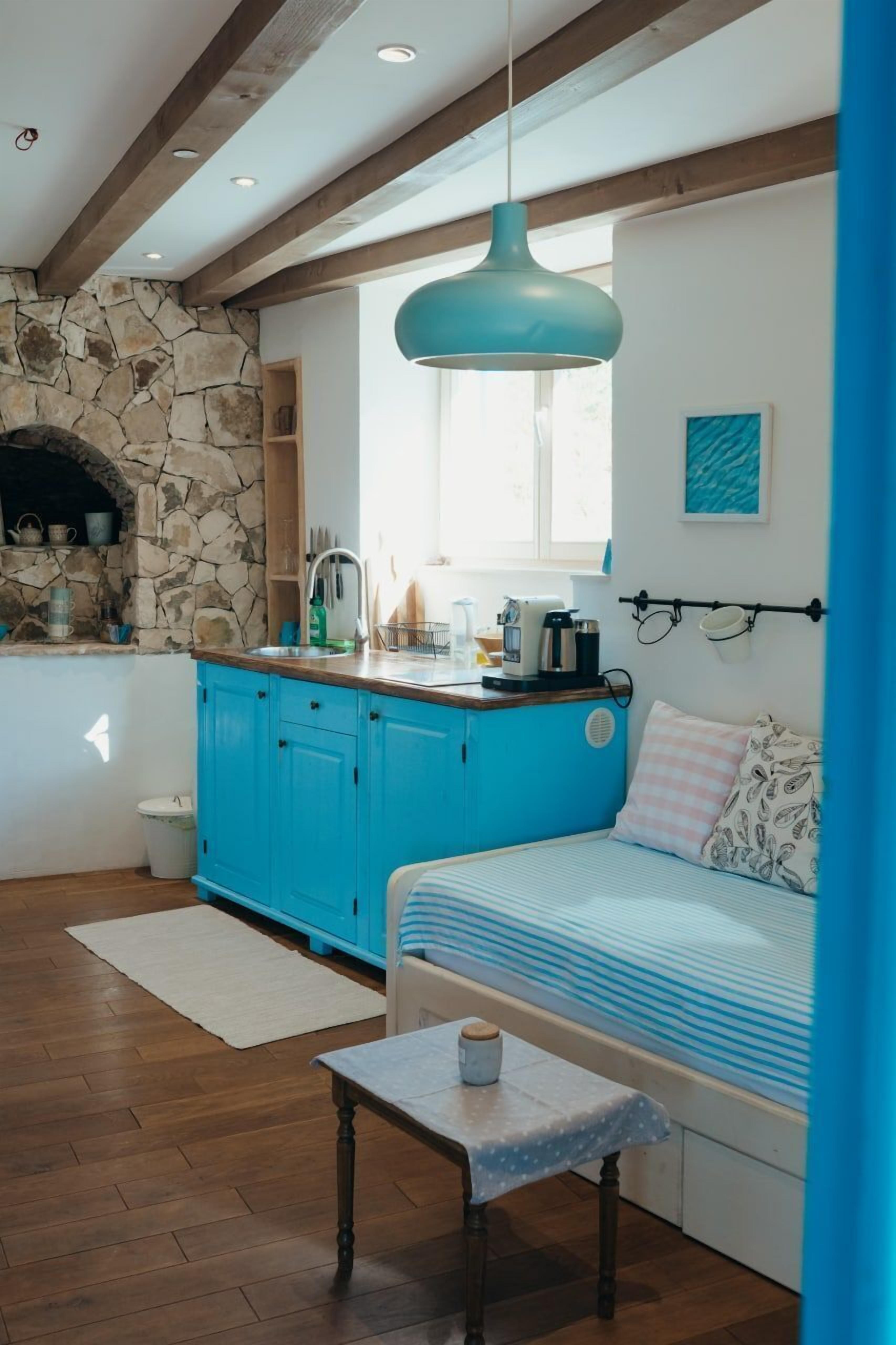 Una cocina acogedora con armarios azules, una pared de piedra y una lámpara colgante.