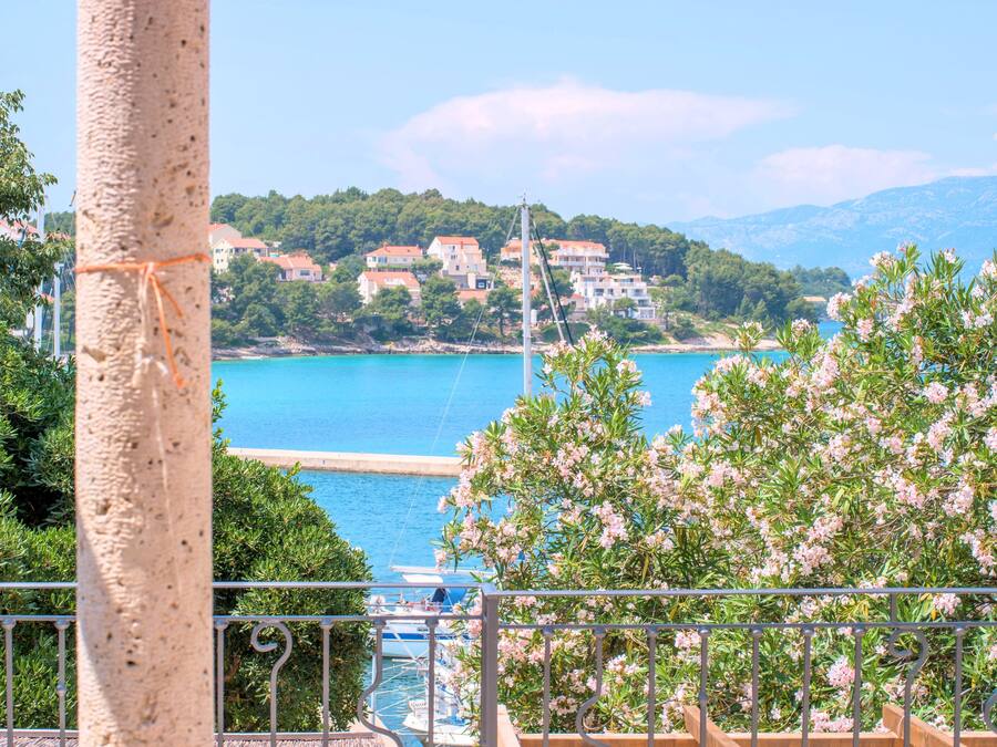 Une vue sur la côte, avec un balcon donnant sur une marina, une mer bleue et limpide, et des bâtiments situés sur une colline.