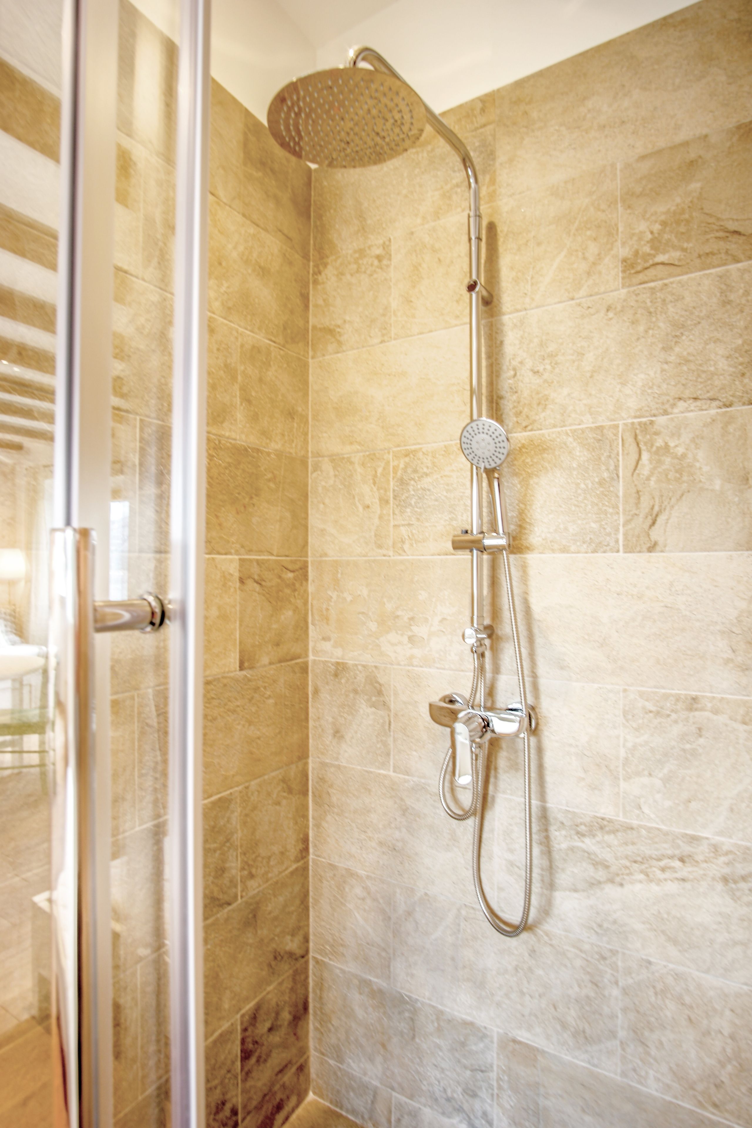 A shower with a handheld showerhead and a wall-mounted control.