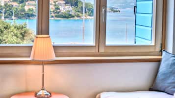 Una habitación con vista a la costa, una lámpara sobre una mesita y una cama con un cojín y un libro.