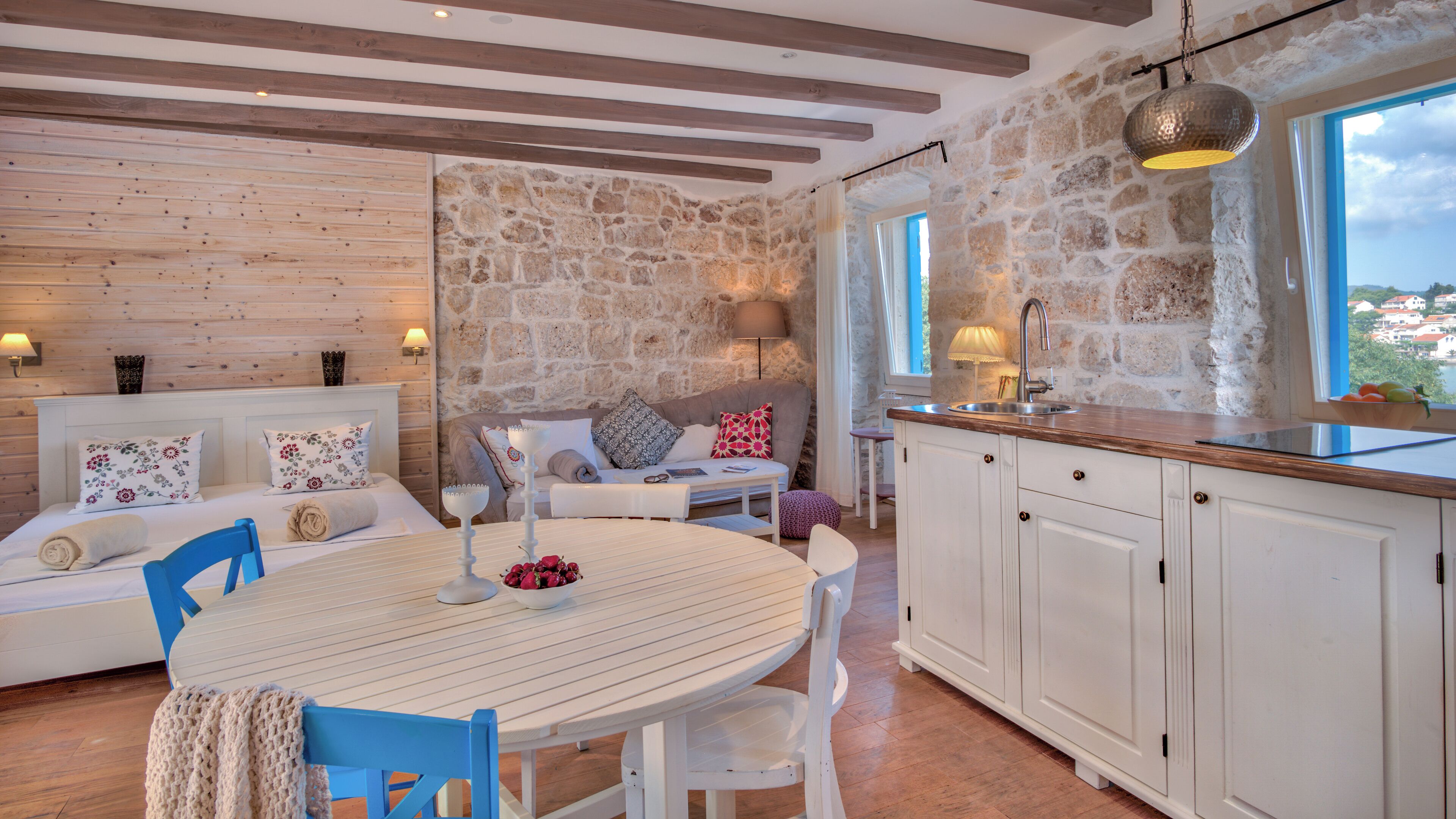 A cozy room with a wooden ceiling, stone walls, a round dining table, and a kitchen area with white cabinets and a sink.