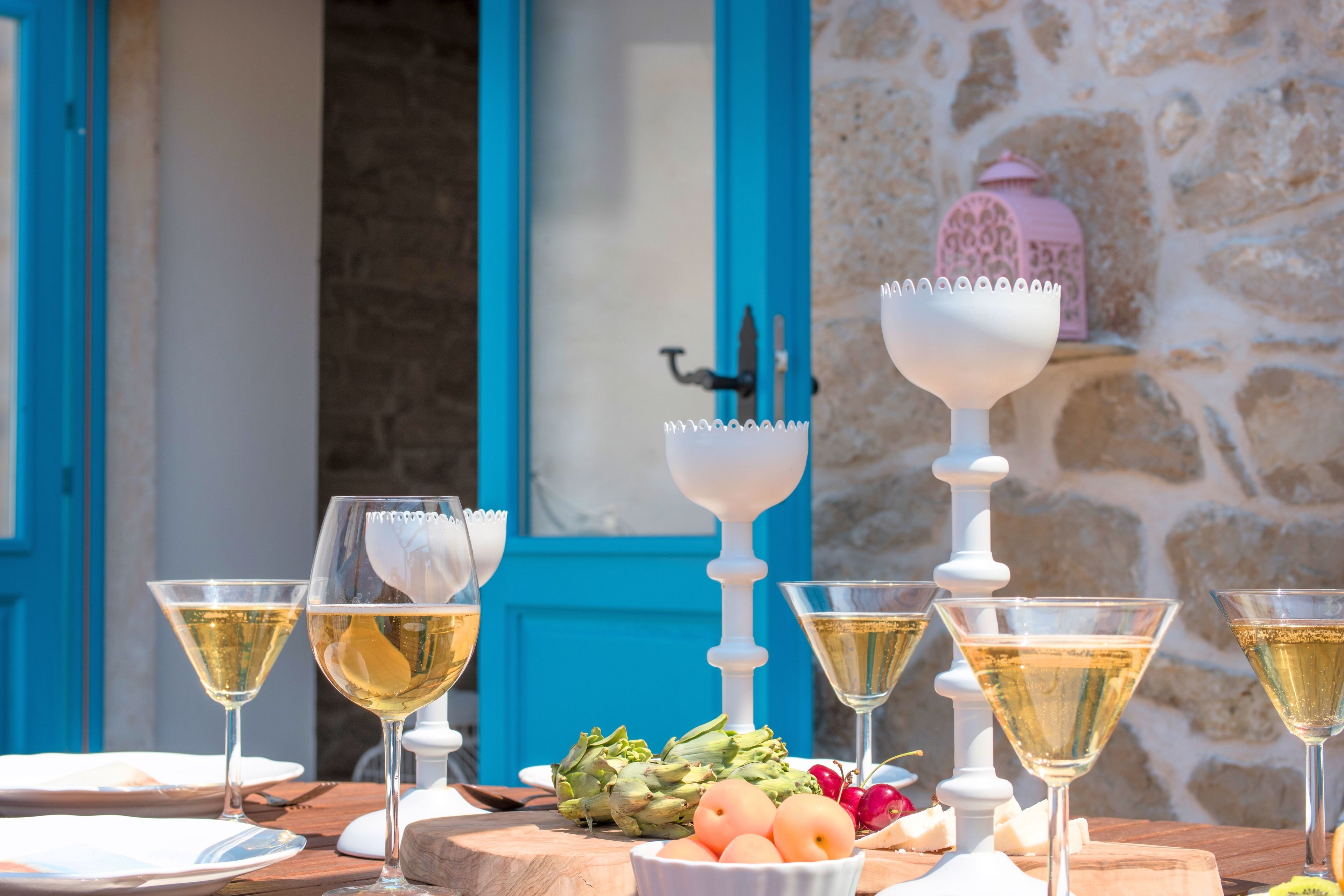 Una mesa dispuesta con copas de vino, un candelabro blanco y un cuenco de fruta.